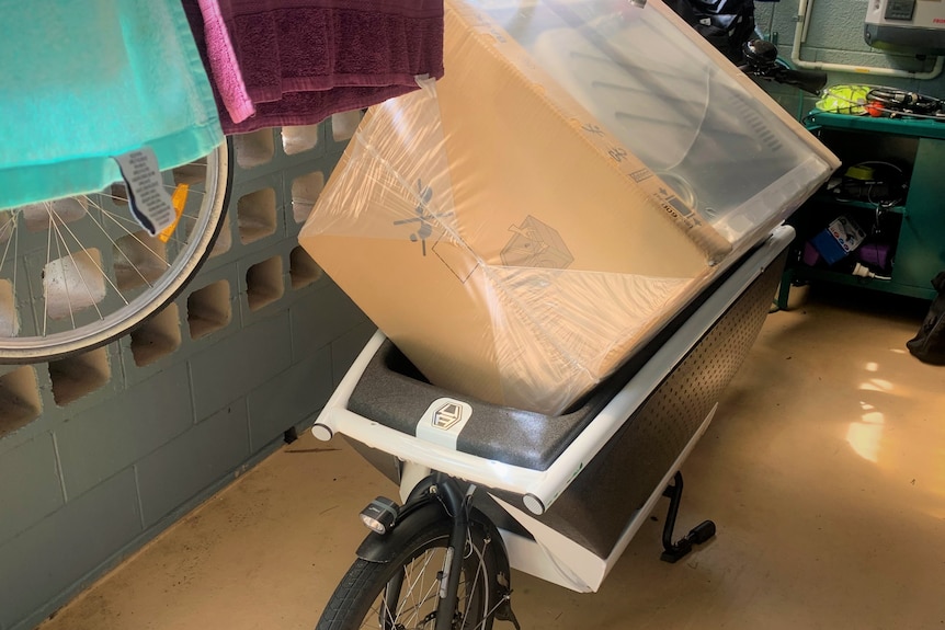 A big brown box on a bike in a townhouse veranda.