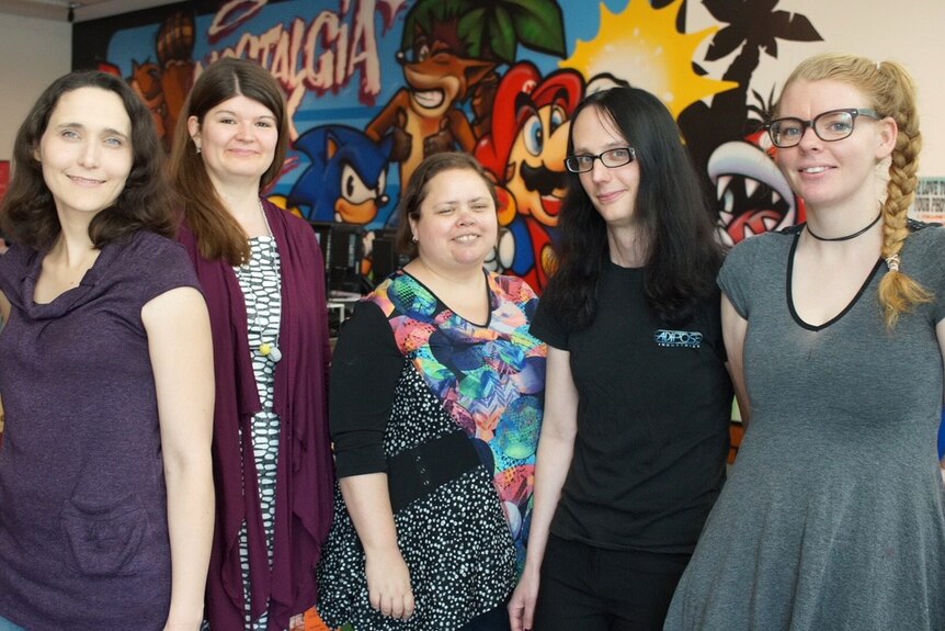 Five women stand side by side in a room posing for a photo.