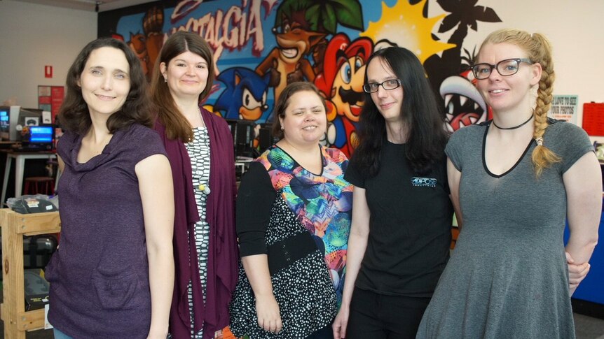 Five women stand side by side in a room posing for a photo.