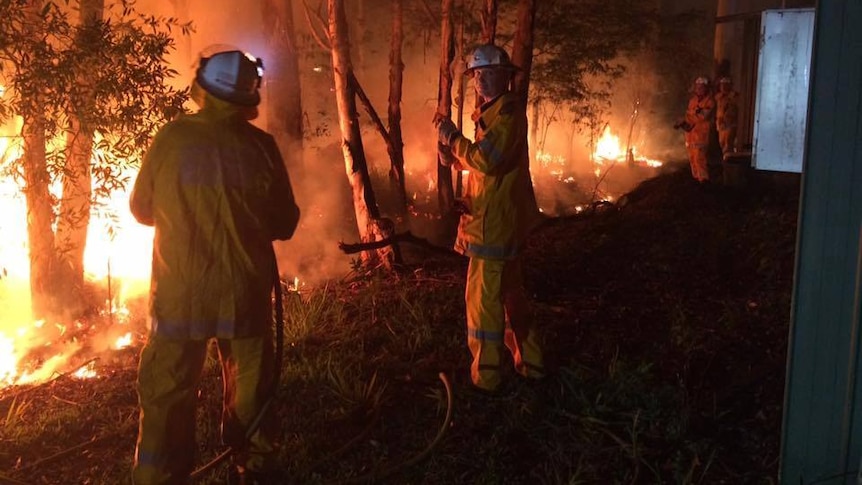 Justin Choveaux stands with another firefighter next to a vegetation fire at night.