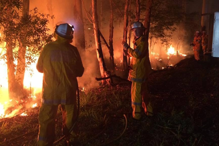 Justin Choveaux stands with another firefighter next to a vegetation fire at night.