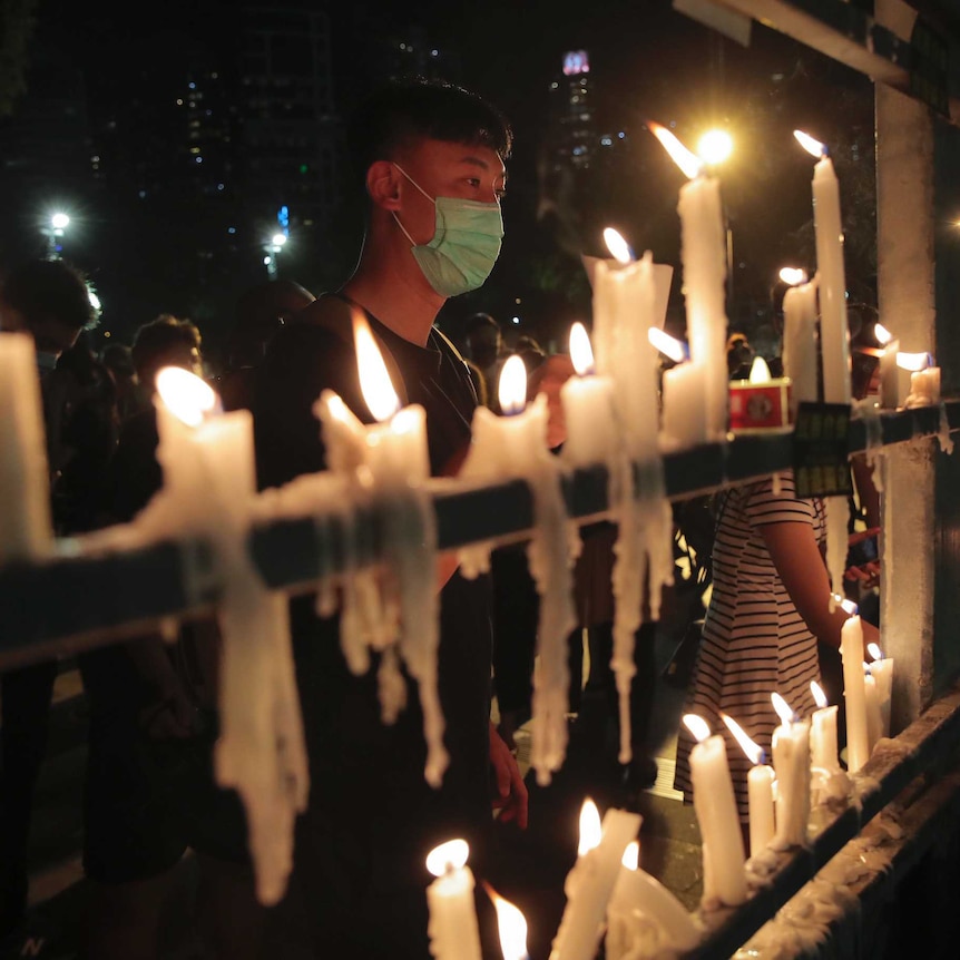 People light a long row of candles as crowds can be seen in the background on a dark night.
