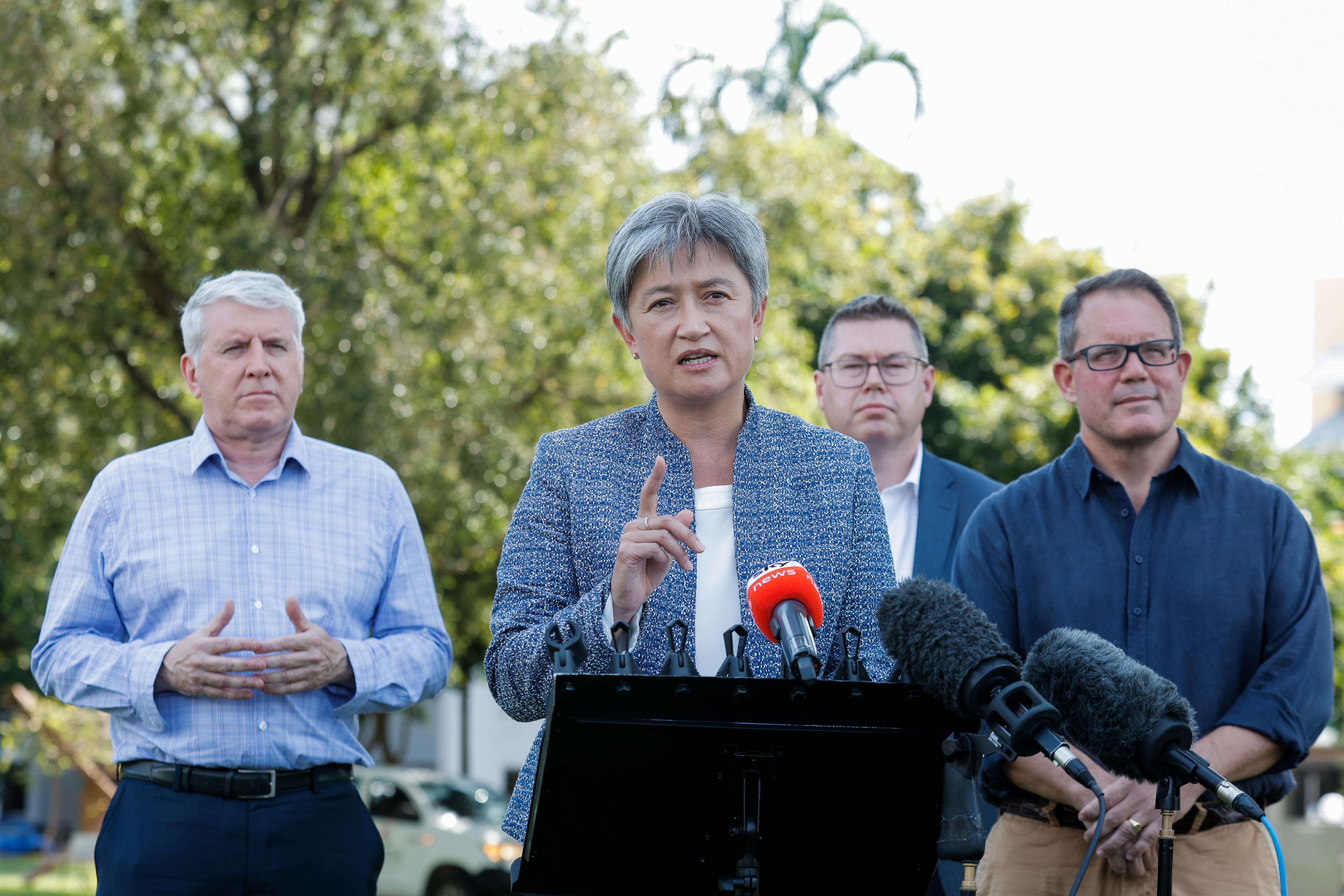 Penny Wong speaks at an outdoor media conference. Three men stand behind her. 