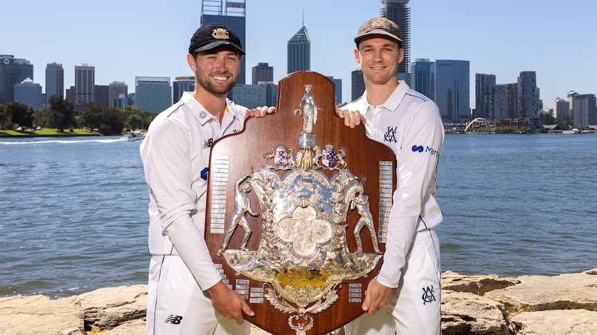 Sam Whiteman of Western Australia and Peter Handscomb of Victoria hold the Sheffield Shield in front of the Perth city skyline.