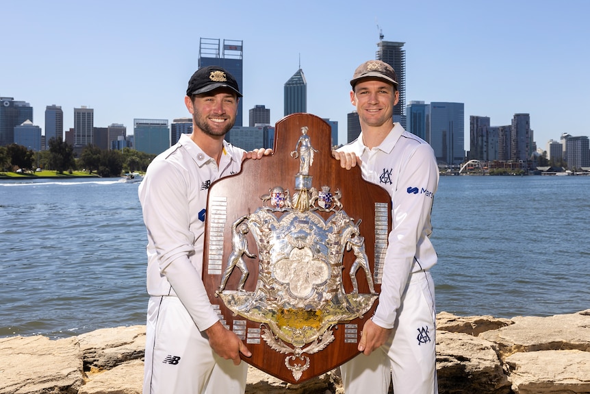 Sam Whiteman of Western Australia and Peter Handscomb of Victoria hold the Sheffield Shield in front of the Perth city skyline.