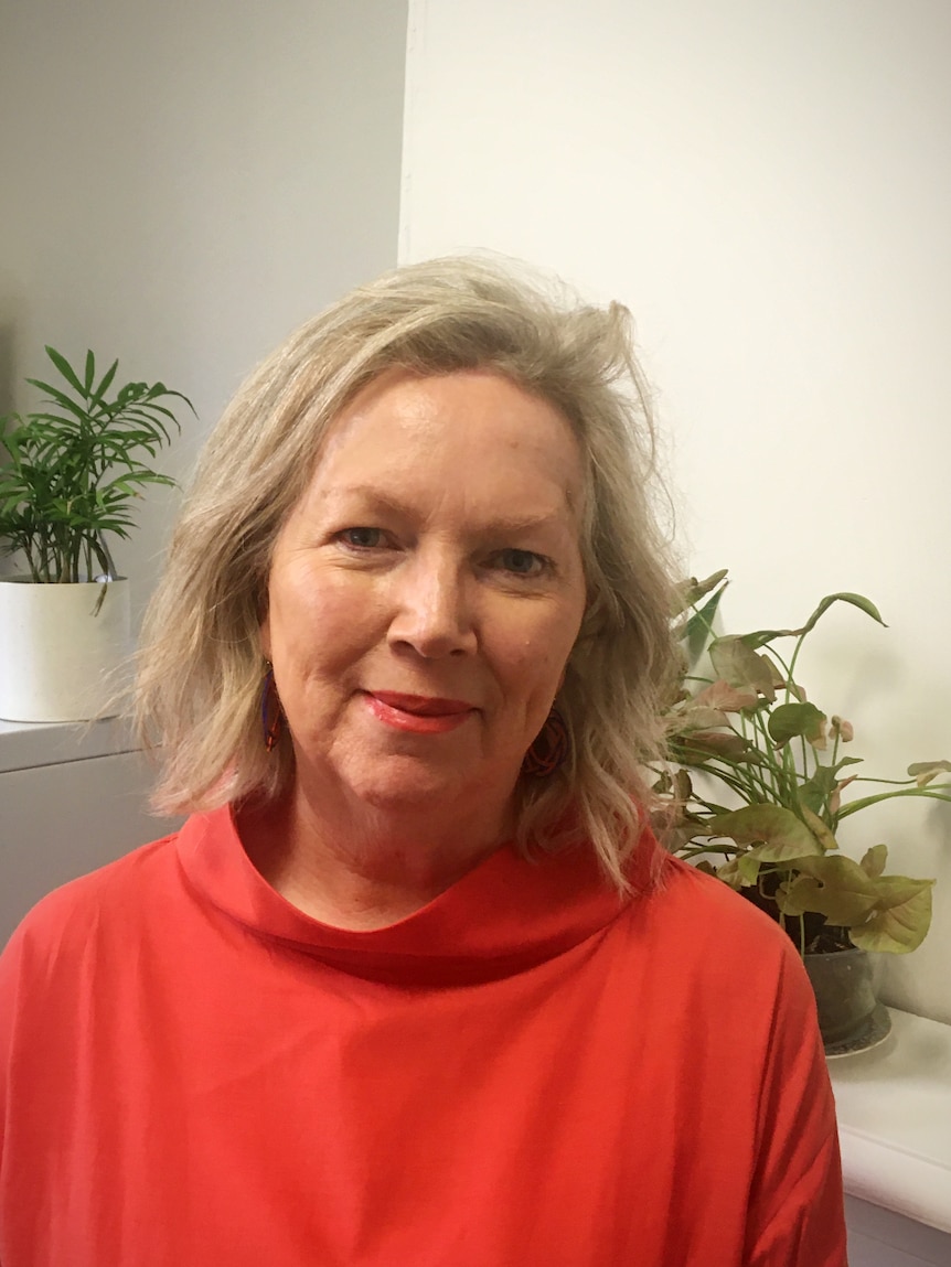 A lady in a red jumper with blonde hair smiles at the camera