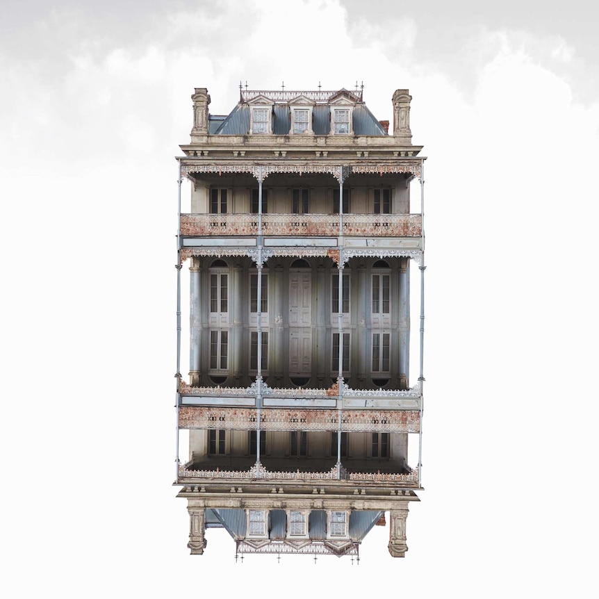 A large old house and its identical reflection floats in front of a grey sky.