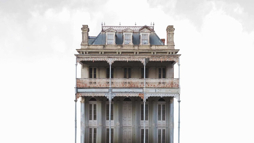 A large old house and its identical reflection floats in front of a grey sky.