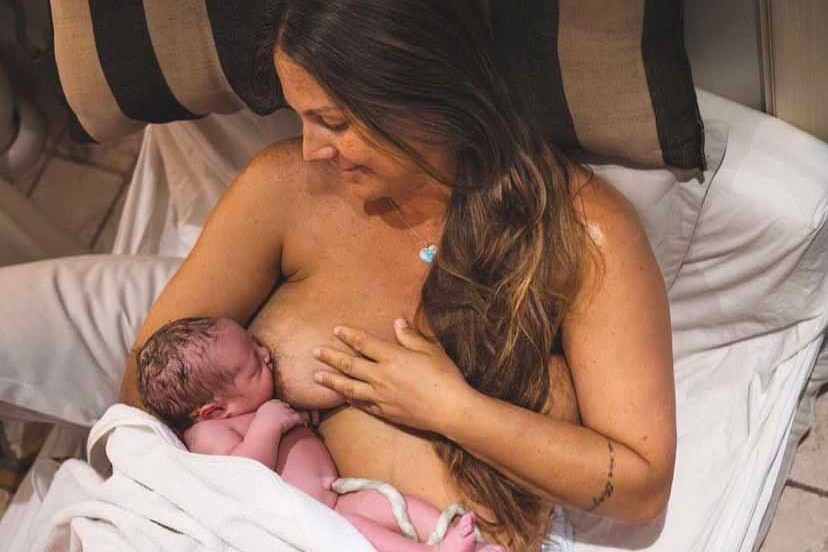 A woman lies in a bed breastfeeding a newborn baby