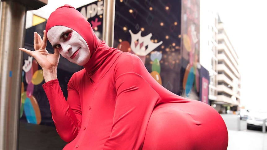 A man in a red suit with fake bottom smiles at the camera.