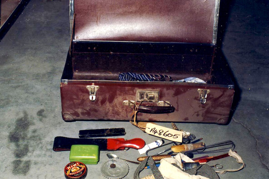 Отворен червен куфар с бял етикет с номера, съдържанието му, включително боя за ботуши, разпръснато по пода.