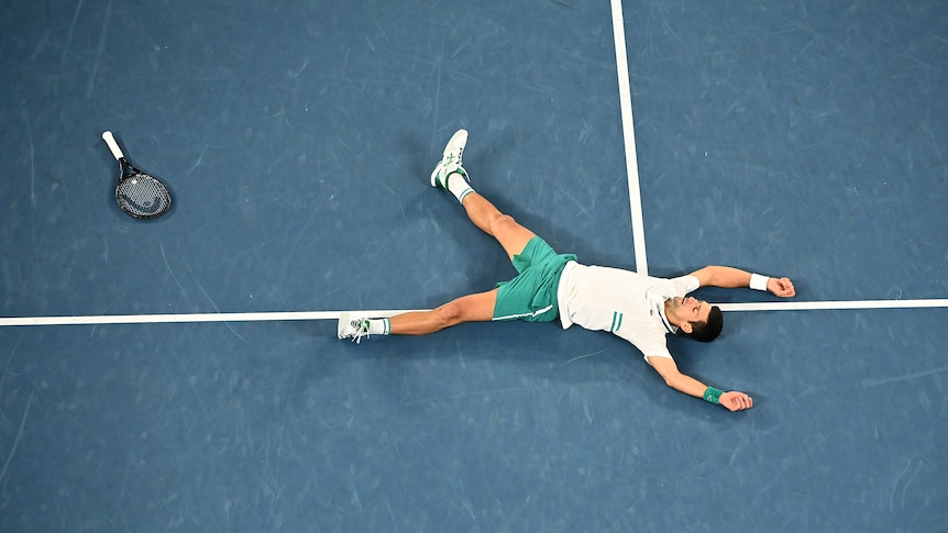 Serbian tennis player Novak Djokovic laying on the tennis court after winning a match