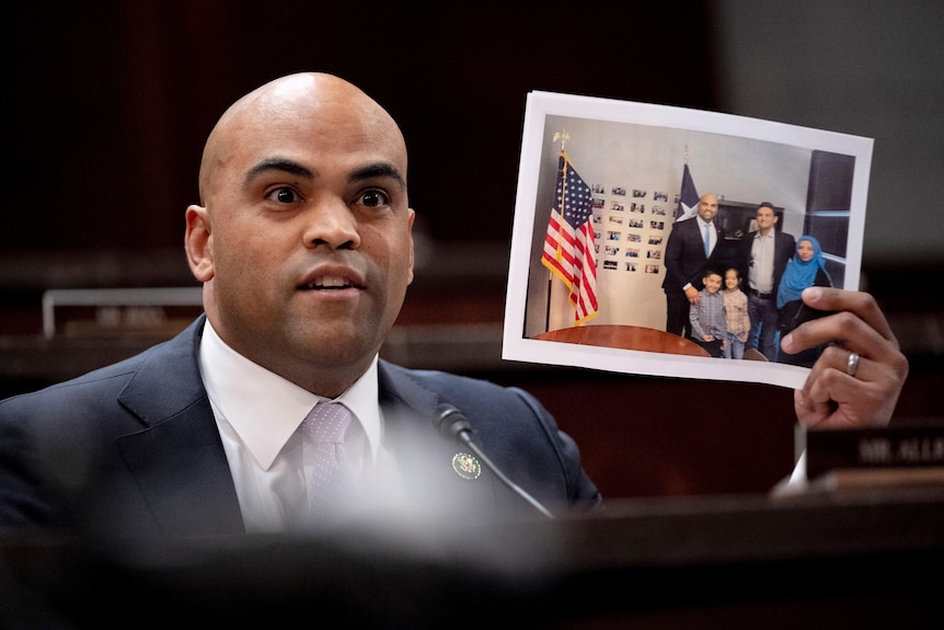 A man holds up a photo of himself and a family standing next to the US flag.