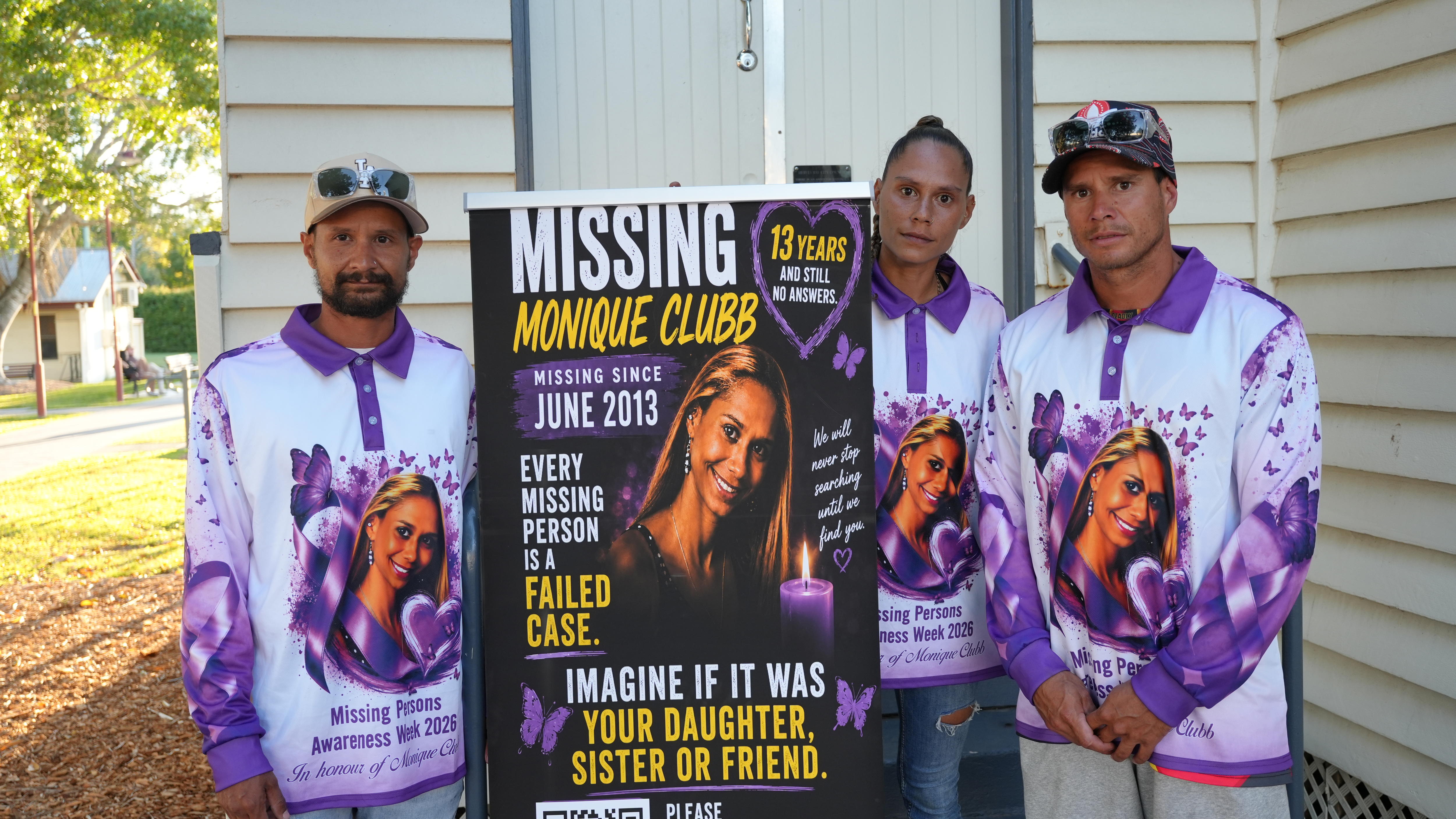 Three siblings wearing matching purple shirts hold up a large poster.