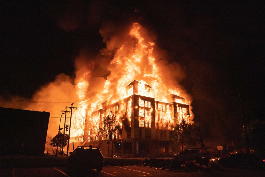 A large building is engulfed in flames in front of a black night sky.