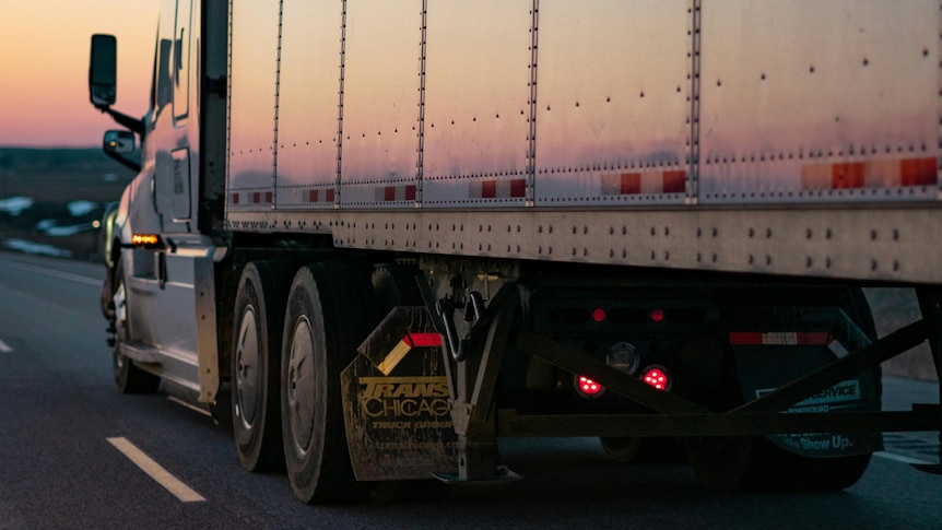A large silver truck drives off into a pink sunset.