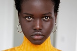 Adut Akech, wearing a yellow knitted top,  looks at the camera in a posed portrait.