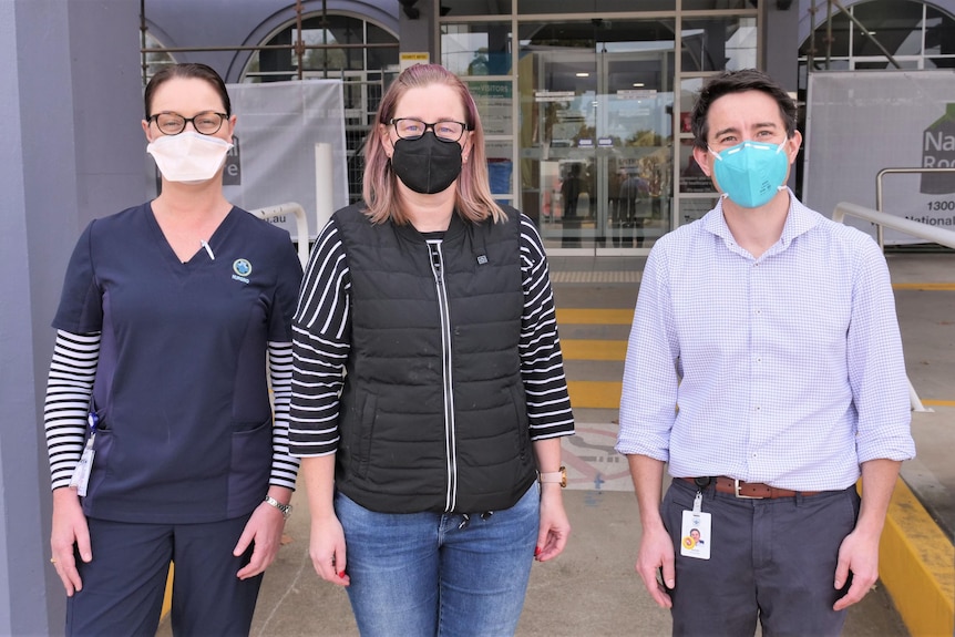 Three people standing next to each other and wearing covid masks out the front of a building