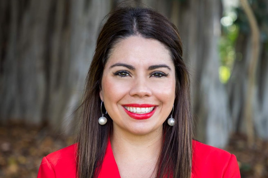 A woman wearing a red jacket smiling in a park in a corporate photo