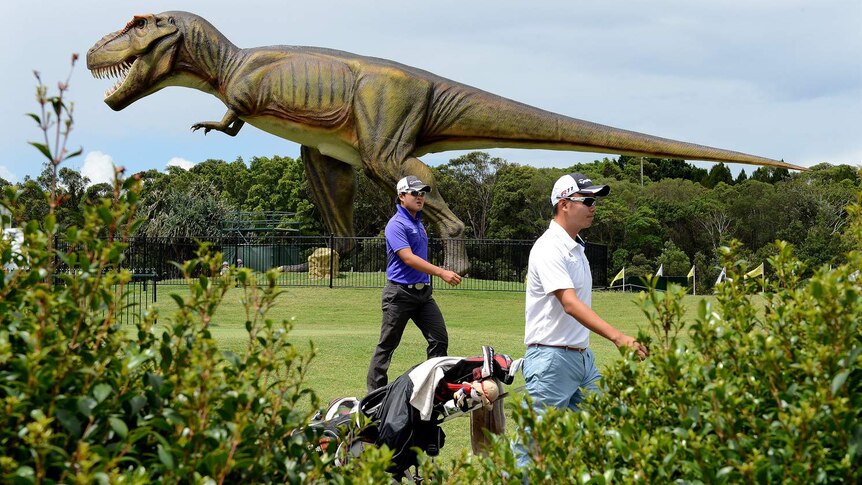 Golfers walk past a giant replica dinosaur on the Australian PGA course at Coolum.