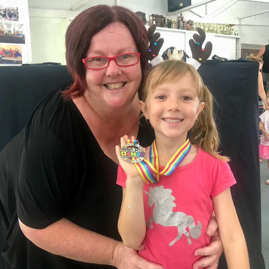 A woman wearing red glasses poses with a blonde girl wearing a medal.