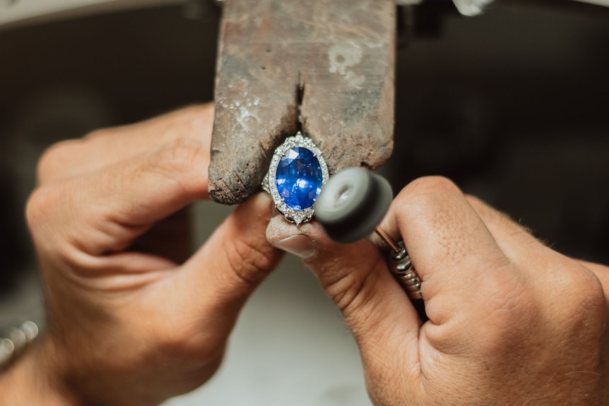 Two hands position a large blue gemstone.