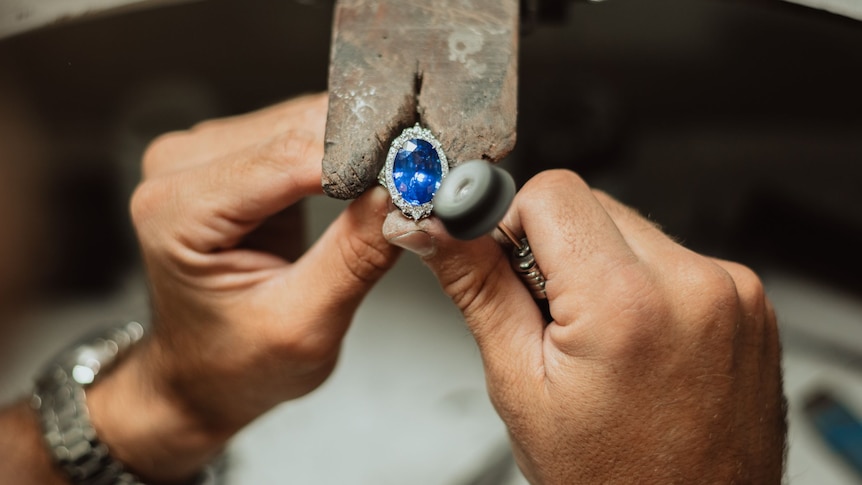 Two hands position a large blue gemstone.