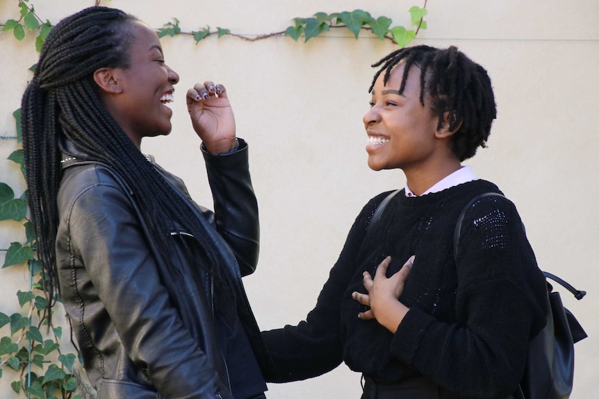 Two young woman laugh together in conversation.