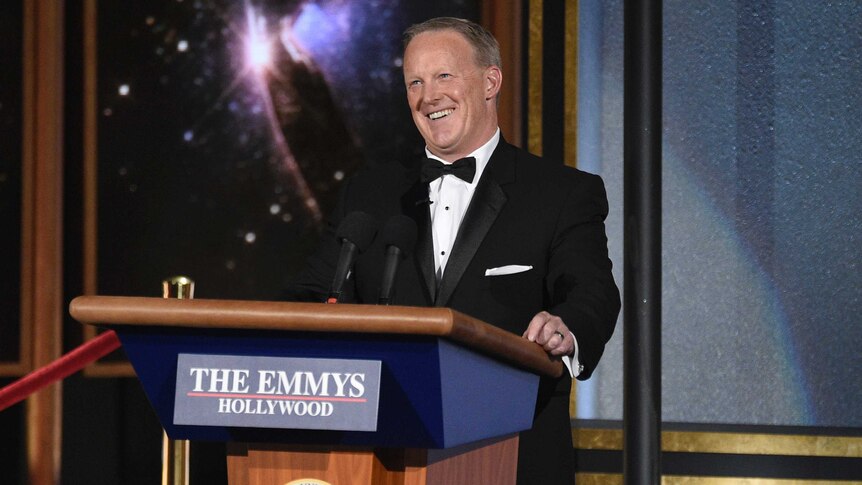 Sean Spicer smiles as he stands behind a podium at the Emmy Awards.