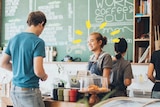 A smiling young woman behind a counter in a busy-looking cafe takes a man's order to depict advice for your first job.