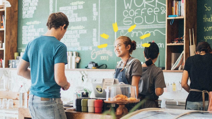 A smiling young woman behind a counter in a busy-looking cafe takes a man's order to depict advice for your first job.