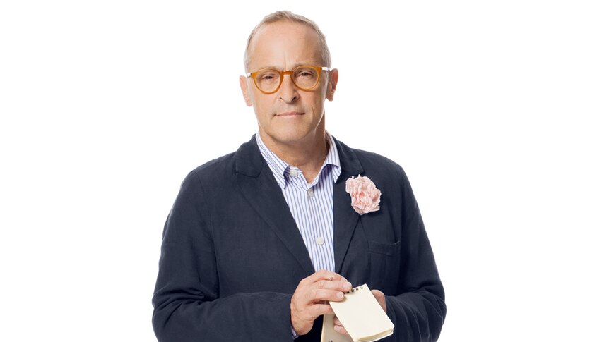 A photo of David Sedaris shows him holding a notebook, a flower on his lapel.