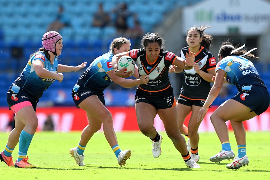 An NRLW player runs forward, holding the ball in one hand and putting her palm out to fend off defenders with the other.