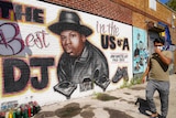 A person wearing a surgical mask walks past a mural of Jam Master Jay in New York.