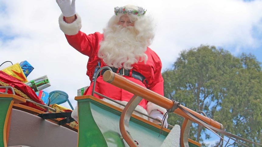 santa claus waves from atop a pageant float