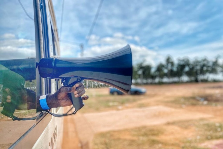 A hand holds a megaphone outside a bus window.