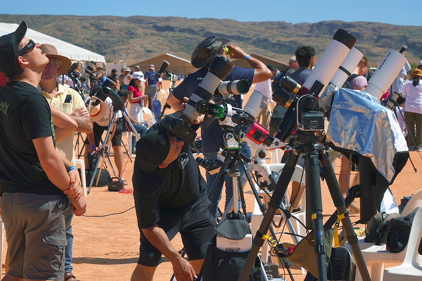People looking through telescopes up at the solar eclipse