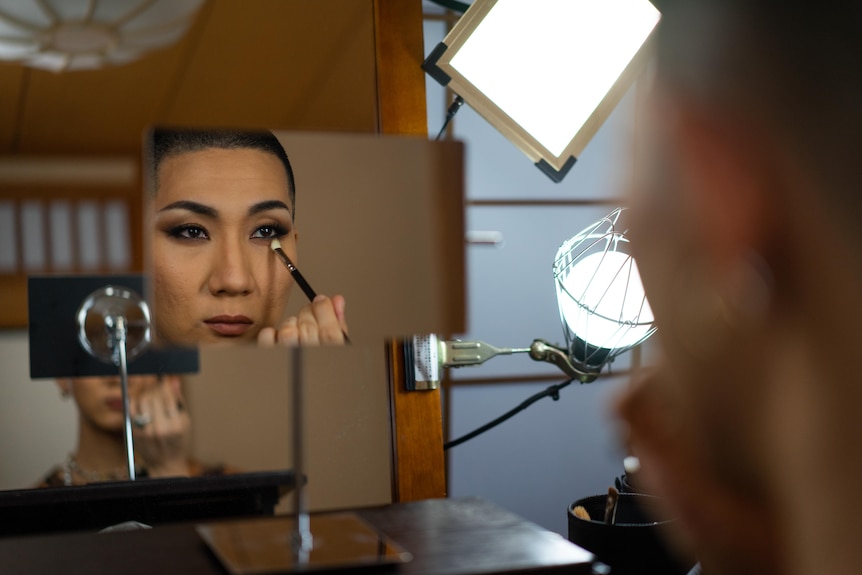Person looking in a mirror and applying eye make up.
