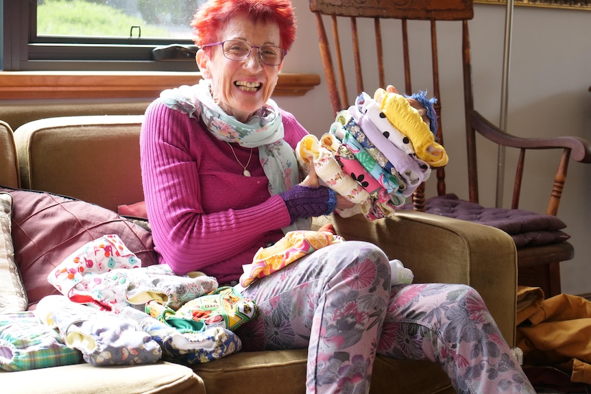 brightly dressed smiling woman holds stack of handmade cloth nappies