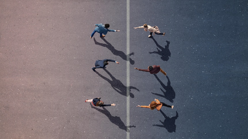 A birds eye view image of 2 groups of people separated by a painted line on the ground. They are reaching towards eachother. 