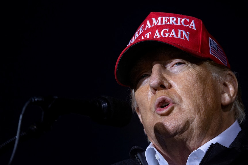 Donald Trump wearing a red 'make America great again' cap while pursing his lips 