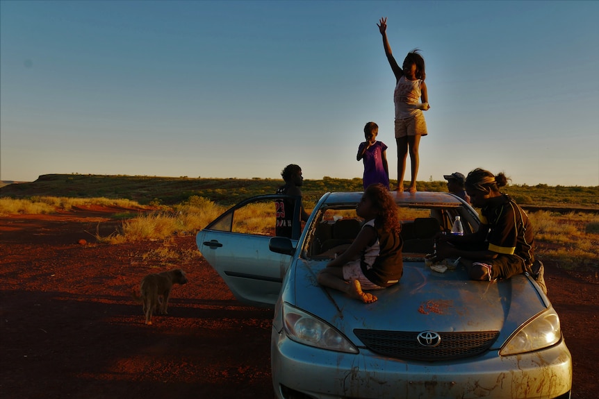 Children sit and stand on top of a car.