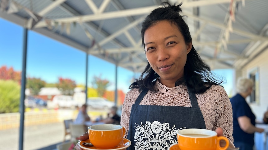 A woman holds two cups of coffee.