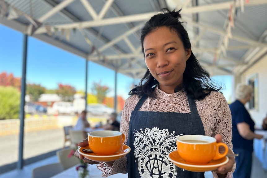 A woman holds two cups of coffee.