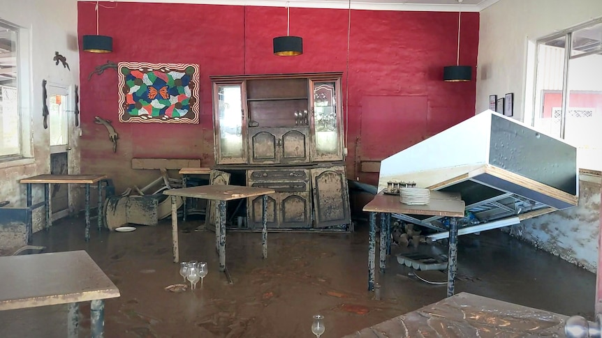 Wine glasses stand upright in brown sludge in a pub devastated by floods