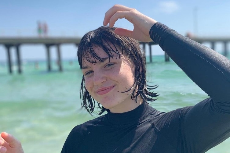 Teenage girl smiling in wetsuit by the water.