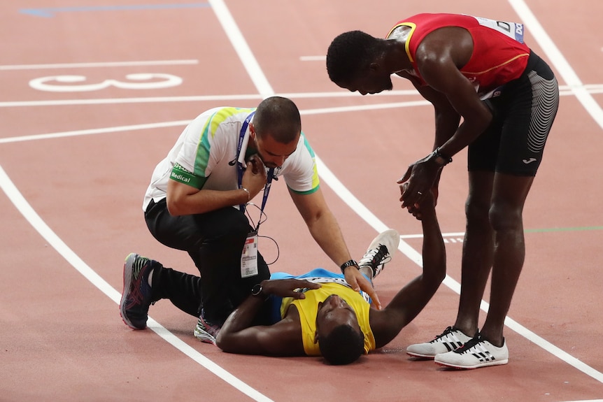 A male athlete lies on the track as he receives medical attention.