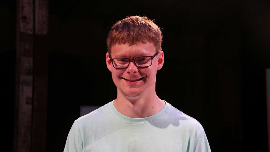 A boy with glasses and red hair smiles at the camera