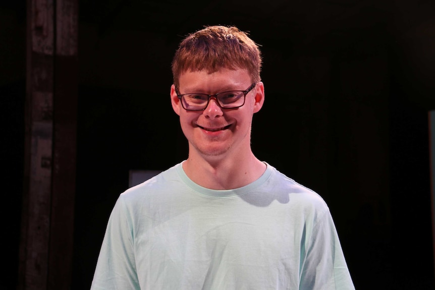 A boy with glasses and red hair smiles at the camera