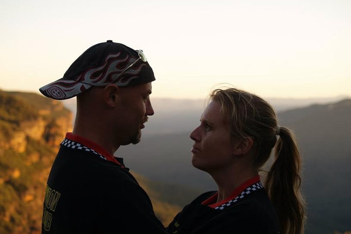 A man and woman look at each other with the blue mountains in the background